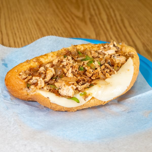 Toasted sub sandwich filled with chopped chicken, melted cheese, sautéed onions, and green peppers on a blue plate.