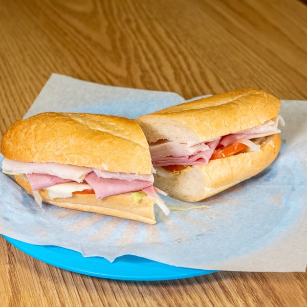 Two deli sandwiches with sliced ham, turkey, cheese, lettuce, tomato, and onions on a blue plate.