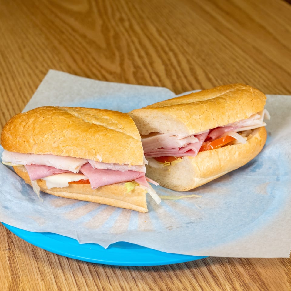 Two deli sandwiches with sliced ham, turkey, cheese, lettuce, tomato, and onions on a blue plate.