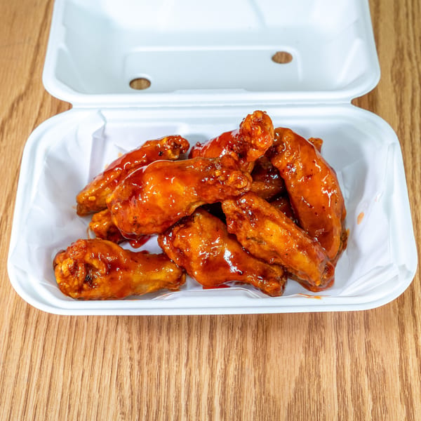 Open takeout container filled with glossy, orange-glazed chicken wings on a wooden table.