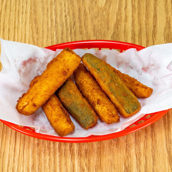 Crispy breaded vegetable sticks arranged in a red paper-lined basket on a wooden table.