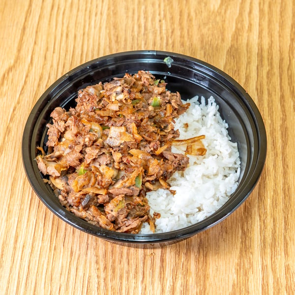 Black bowl of sautéed beef, onions, mushrooms, and peppers served with white rice on a wooden table.