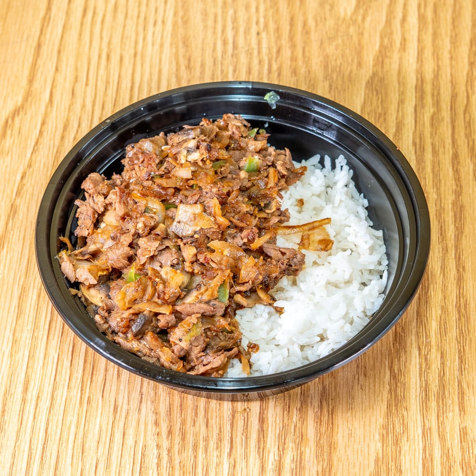 Black bowl of sautéed beef, onions, mushrooms, and peppers served with white rice on a wooden table.