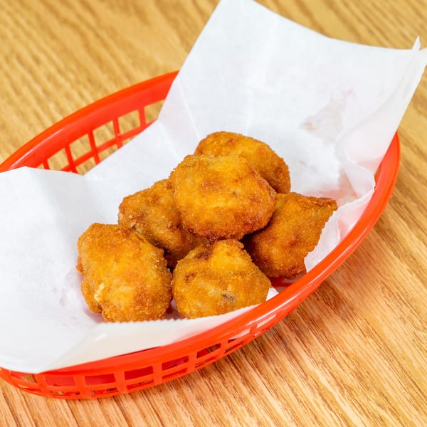 Basket of golden-brown breaded fried bites lined with white paper on a wooden restaurant table.