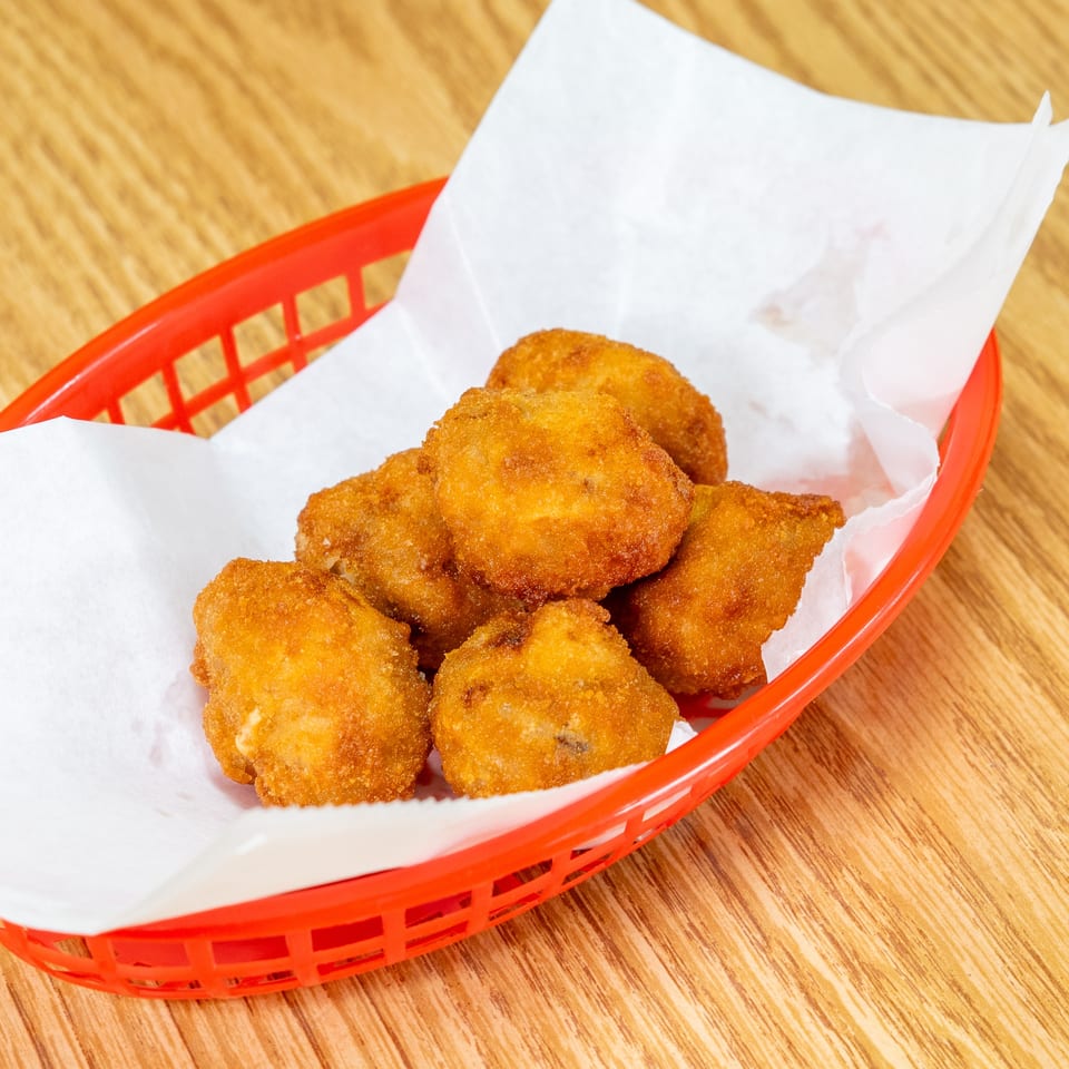 Basket of golden-brown breaded fried bites lined with white paper on a wooden restaurant table.
