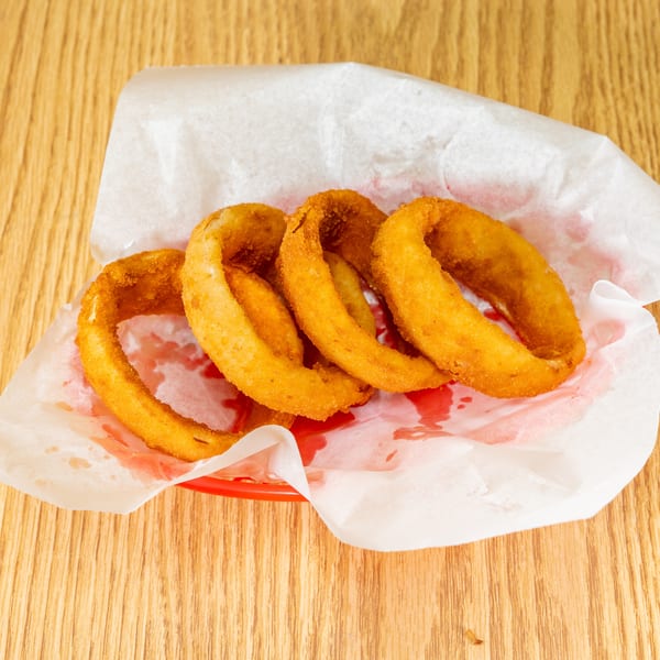 Crispy golden onion rings served in a paper-lined basket with ketchup on a wooden table.